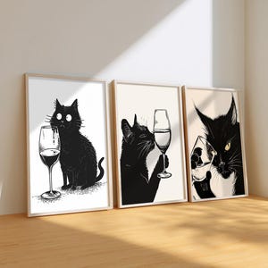Peut inclure: Ensemble de trois impressions encadrées représentant des chats noirs avec des verres de vin. Les illustrations en noir et blanc présentent un style minimaliste. Un chat renverse du vin. Les cadres sont en bois clair.