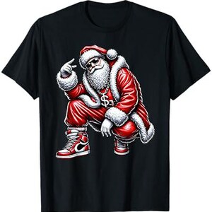 Op de afbeelding: Een zwart T-shirt met een afbeelding van de kerstman in een rood pak, een gouden ketting en sneakers. Hij zit in een hurkende houding met zijn hand omhoog in een peace-teken.