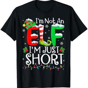 以下が含まれることがあります： クリスマスのエルフのデザインが施された黒いTシャツ。テキストは「I'm Not An Elf I'm Just Short」と書いてあり、緑と赤の文字で、クリスマスの電飾が飾られています。