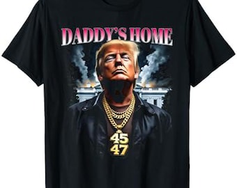 May include: Black t-shirt with a graphic of Donald Trump wearing a gold chain with the numbers 45 and 47. The text "Daddy's Home" is above the image.
