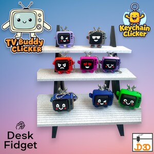 Puede incluir: Una exhibición de coloridos fidgets de escritorio y llaveros TV Buddy Clicker. Cada televisor en miniatura tiene una expresión y un color únicos, incluyendo morado, negro, rojo, rosa, azul y verde. También presenta el texto "TV Buddy Clicker", "Keychain Clicker" y "Desk Fidget".