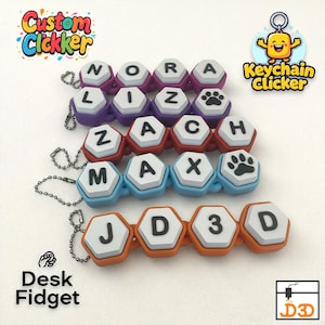 Op de afbeelding: Aangepaste clicker sleutelhangers en bureau fidgets in diverse kleuren. Elke clicker heeft zeshoekige tegels met letters, cijfers en pootafdrukken. De teksten "Custom Clickker", "Keychain Clicker", "Desk Fidget" en "D3D" zijn zichtbaar.