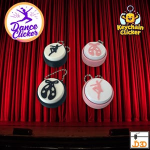 May include: Four keyrings labelled "Keychain Clicker" with ballet-themed designs. Each keyring has a round, white top with a ballet dancer or shoe silhouette in black or pink. The keyrings are set against a red curtain backdrop.