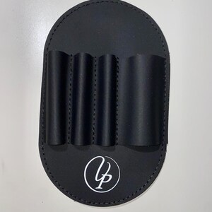 May include: Black leather case with five slots for holding lipstick tubes. The case has a white circle with the letters "VP" in the centre.