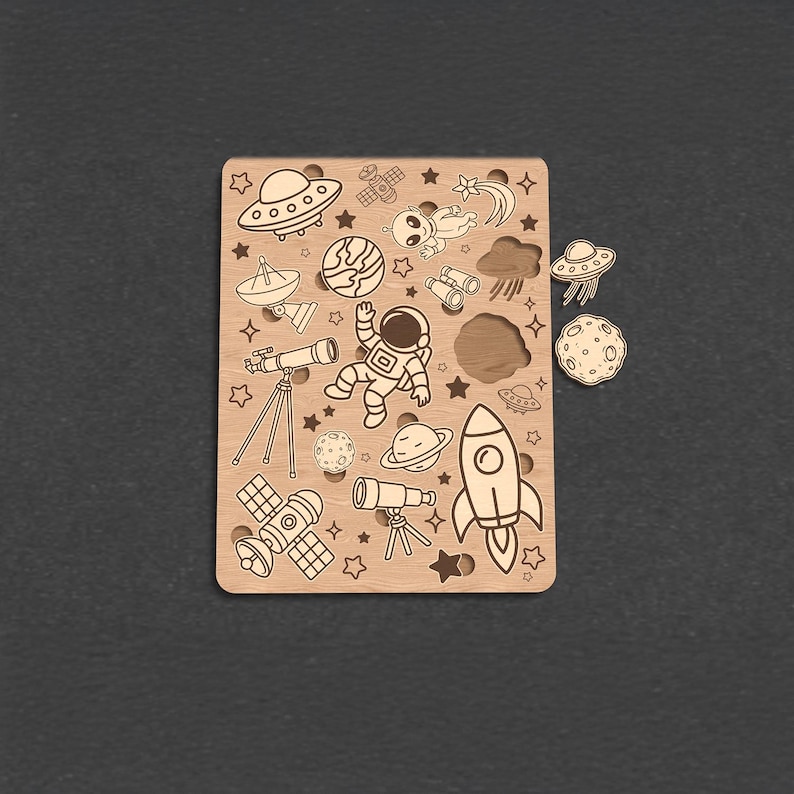 Op de afbeelding: Houten puzzel met ruimtethema met verschillende illustraties, waaronder een raket, planeten, een astronaut en UFO's. De puzzelstukjes zijn los van het hoofdbord, dat uitgesneden vormen heeft. De puzzel is gemaakt van lichtgekleurd hout.