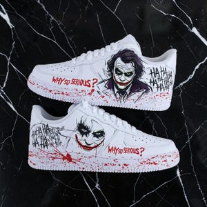 Può includere: Sneakers bianche con un design a tema Joker. Le scarpe mostrano la frase "WHY SO SERIOUS?" e una grafica del volto del Joker. Schizzi di vernice rossa accentuano il design, con il testo "HA HA HA HA".
