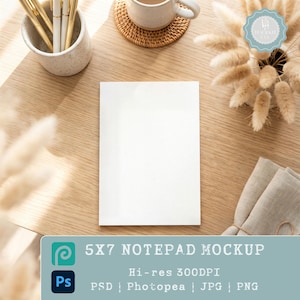Puede incluir: Una maqueta de bloc de notas de 5x7 sobre una superficie de madera, con una taza de café, bolígrafos y elementos decorativos. El bloc de notas es blanco y en blanco, listo para el diseño. La imagen incluye el texto "5X7 NOTEPAD MOCKUP" y "Hi-res 300DPI".