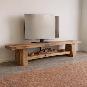 May include: A rustic, wooden TV stand with a lower shelf and angled legs. The stand is made of light-colored wood and features a natural finish. A flat-screen TV sits on top. The stand is 72 inches long.