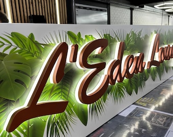 May include: A white sign featuring the text L'Eden Lounge in raised, metallic copper-colored script lettering with integrated backlighting, set against a vibrant background of green tropical palm and monstera leaves.