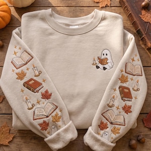 Puede incluir: Una sudadera de cuello redondo en color beige con bordados en el pecho y las mangas. En el pecho aparece un pequeño fantasma leyendo un libro junto a una vela. Las mangas presentan motivos de libros abiertos, cerrados, velas, hojas de arce y fantasmas.