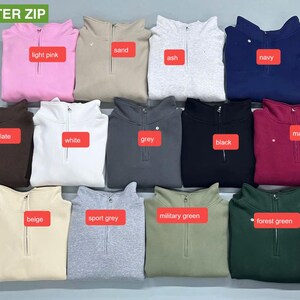 May include: A collection of quarter-zip sweatshirts in various colors, including light pink, sand, ash, navy, dark chocolate, maroon, white, grey, black, beige, sport grey, military green, and forest green. Each sweatshirt has a zipper closure.