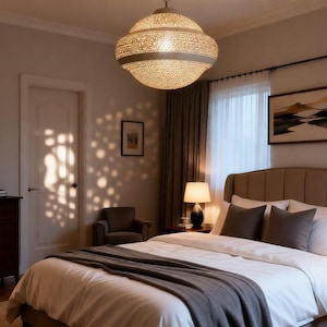 Peut inclure: Intérieur de chambre avec un lit avec une couette blanche et une couverture grise. Des tables de chevet avec des lampes encadrent le lit. Un grand luminaire décoratif est suspendu au plafond. Des œuvres d'art et une horloge ornent les murs.