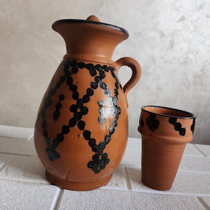 Puede incluir: Una jarra de barro marrón con un diseño geométrico negro y una taza de barro marrón a juego. La jarra tiene una tapa y un asa.