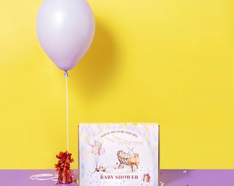 May include: A purple balloon with a string attached to it is floating above a box with a colourful design. The box has the words "Baby Shower" printed on it. There is confetti on a purple surface.