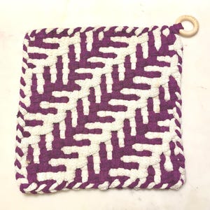 May include: Purple and white woven pot holder with a wooden loop handle.