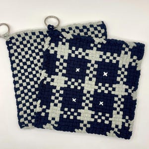 May include: Two gray and navy blue woven pot holders with a checkered pattern and white X's. The pot holders have metal loops for hanging.