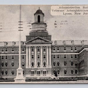 May include: A black and white vintage postcard showing the Administration Building at the Veterans Administration Facility in Lyons, New Jersey. The multi-story brick building features a central tower, a pediment, and numerous windows.