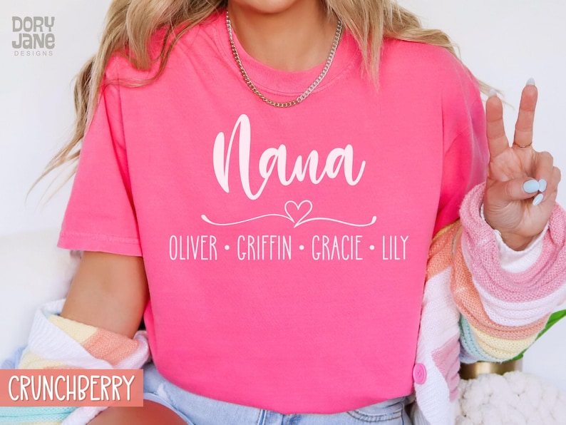 May include: Pink t-shirt with the text "Nana" in white cursive font, a small white heart, and the names "Oliver, Griffin, Gracie, Lily" in white text below.