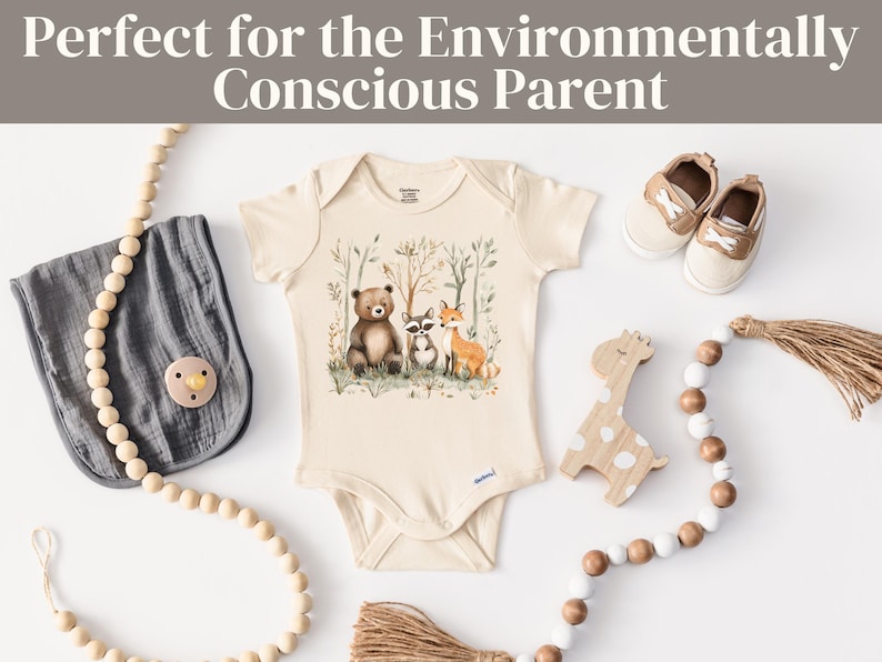 May include: A cream-colored baby onesie with a woodland animal print featuring a bear, raccoon, and fox. The onesie is surrounded by wooden beads and a wooden giraffe toy.