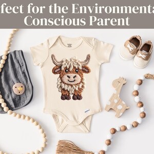 Pode incluir: Body de beb&eacute; creme com um design bordado de vaca Highland. A imagem inclui um babete cinzento, uma girafa de madeira, uma chupeta, sapatos e uma grinalda de contas de madeira. O texto na parte superior diz "Perfect for the Environmentally Conscious Parent."
