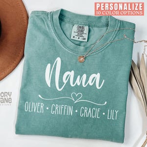 May include: A teal blue t-shirt with the word "Nana" in white text and a heart design. Below the word "Nana" are the names "Oliver, Griffin, Gracie, Lily" in white text.
