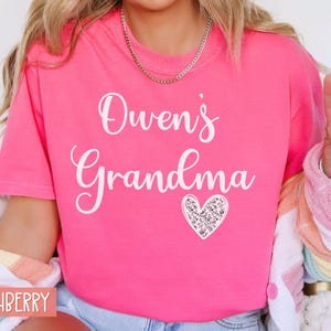 May include: Pink t-shirt with the text "Owen's Grandma" in white lettering and a sparkly silver heart.