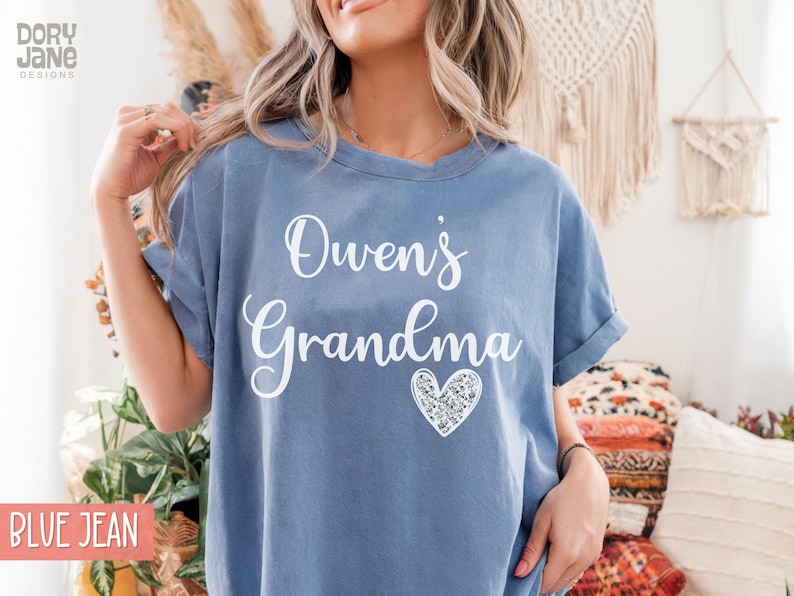 May include: A blue jean t-shirt with the text "Owen's Grandma" in white lettering and a sparkly silver heart.