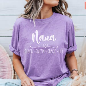 May include: A purple t-shirt with the text "Mama" in white cursive lettering. Below the text is a small heart and the names "Oliver, Griffin, Gracie, Lily" in white.