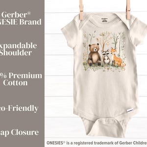 May include: A beige Gerber Onesie&reg; bodysuit with a woodland animal print featuring a bear, raccoon, and fox. The text "Dory Jane Designs" is printed on the right side of the image. The Onesie&reg; has an expandable shoulder and snap closure.