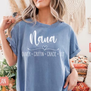May include: A blue jean t-shirt with the word "Nana" and a heart design. Below the word "Nana" are the names "Oliver, Griffin, Gracie, Lily". The t-shirt is labeled "Super Soft".