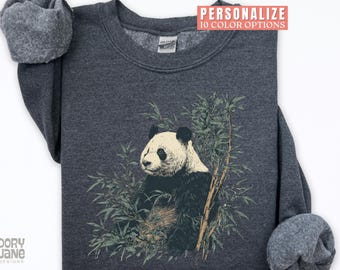 May include: Dark gray sweatshirt featuring a panda bear illustration surrounded by bamboo. The panda has black and white fur. The sweatshirt has the text "PERSONALIZE 10 COLOR OPTIONS" in a pink rectangle. The brand name "DORY JANE DESIGNS" is at the bottom.