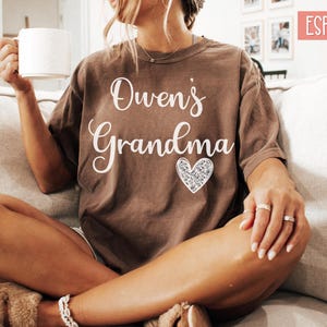 May include: A brown t-shirt with the text "Owen's Grandma" in white lettering and a sparkly silver heart.
