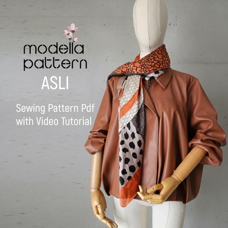 May include: A brown leather jacket with a zipper closure is displayed on a mannequin. A patterned scarf with orange, black, and white designs is draped around the mannequin's neck. The text "modella pattern ASLI" and "Sewing Pattern Pdf with Video Tutorial" are visible.