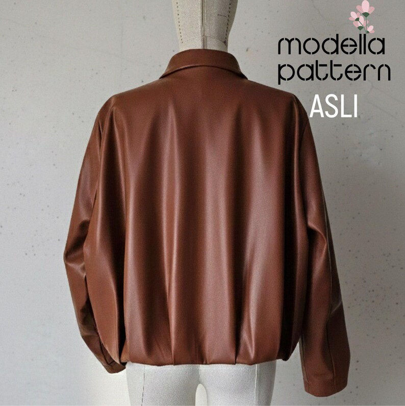 May include: A brown leather jacket with a collared neckline and long sleeves. The jacket has a gathered hem and the text "modella pattern ASLI" is visible on the upper right corner.