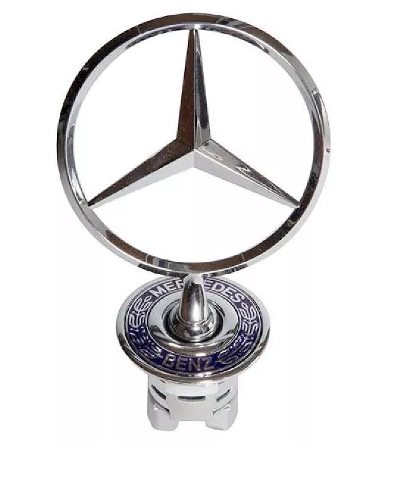 May include: A chrome Mercedes-Benz hood ornament featuring the iconic three-pointed star within a circular frame. The base has a blue and silver emblem with the words "Mercedes Benz".