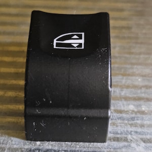 May include: Black plastic car window switch with a white up and down arrow icon.