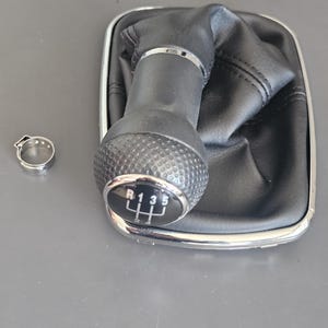 May include: Black leather gear shift knob with a chrome ring and a 5-speed gear pattern. The knob has a textured surface and the gear pattern is labeled with the numbers 1, 3, and 5, and the letter R.