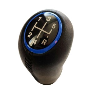 May include: A black gear shift knob with a textured surface and a central circular inlay. The inlay features a glossy black background with white gear position markings for 1, 2, 3, 4, 5, and R, surrounded by a vibrant blue circular trim ring.