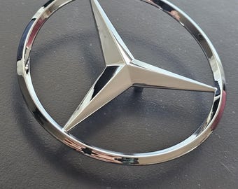 Peut inclure: Un emblème Mercedes-Benz chromé avec une étoile à trois branches au centre.