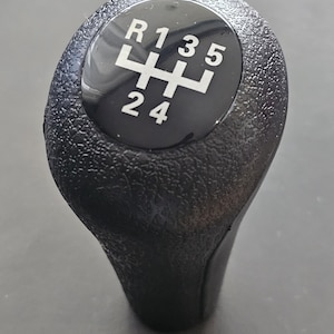 以下が含まれることがあります： 白いギアパターンとR、1、3、5、2、4の数字が書かれた黒いギアノブ