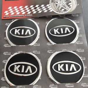 May include: Four black and silver Kia wheel center caps. The caps have a black background with the Kia logo in silver. The packaging reads "METAL SERIES" and "AUTO ACCESSORIES TUNING".