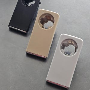 Op de afbeelding: Drie kunststof deurgrepen in zwart, beige en wit. Elke greep heeft een rond gat in het midden en een zilveren rand aan de randen.