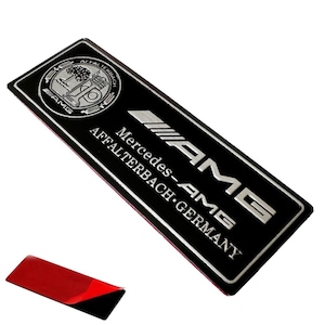 May include: Silver and black Mercedes-AMG emblem with the text "Mercedes-AMG Affalterbach Germany".