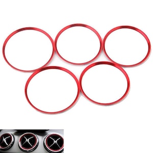 Può includere: Un set di cinque anelli circolari rossi progettati come finiture decorative per le bocchette di ventilazione dei veicoli. Ogni anello presenta una finitura metallica rossa liscia e sottile con un centro vuoto per incorniciare le bocchette.