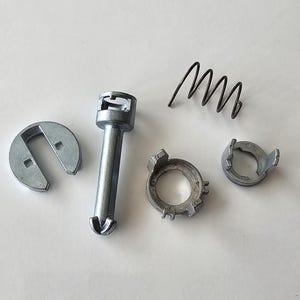 May include: A collection of silver-colored automotive parts, including a cylindrical pin, a spring, and several circular components with various shapes and cutouts. The parts are arranged on a white surface.