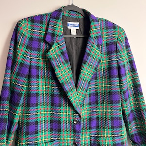 May include: A Pendleton plaid blazer in a vibrant pattern of green, purple, red, and yellow. The jacket features a classic notched collar, two black buttons, and a black lining. The blazer is hanging on a black hanger.