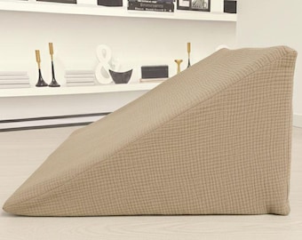 May include: A beige wedge-shaped pillow featuring a textured, grid-like fabric surface. The pillow has a triangular profile with a flat base and a slanted top side, designed to provide an inclined support surface for resting or sitting upright.