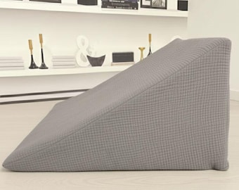 May include: A wedge-shaped pillow with a textured, light gray fabric cover. The pillow features a sloped design that rises from a thin edge to a taller, vertical back panel, providing a firm, triangular profile for support and positioning.