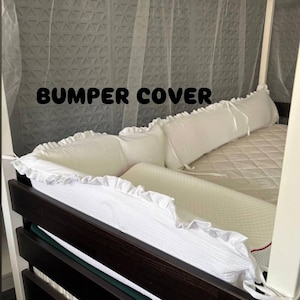 May include: White bumper cover with a ruffled edge, designed for a bed. The text "BUMPER COVER" is displayed in black. The bed frame is dark brown, and the canopy frame is white.
