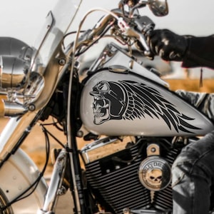 Könnte beinhalten: Ein schwarz-weißes Motorrad-Tank-Dekor mit einem Totenkopf, der einen Helm und eine Fliegerbrille mit einem Federdesign trägt.